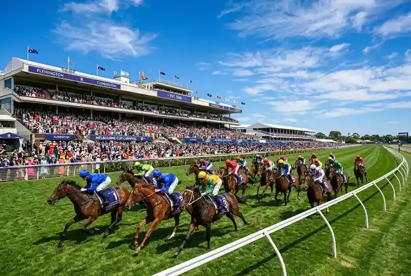 Packed grandstand at Flemington Racecourse on Melbourne Cup day with horses racing on the turf track in the foreground